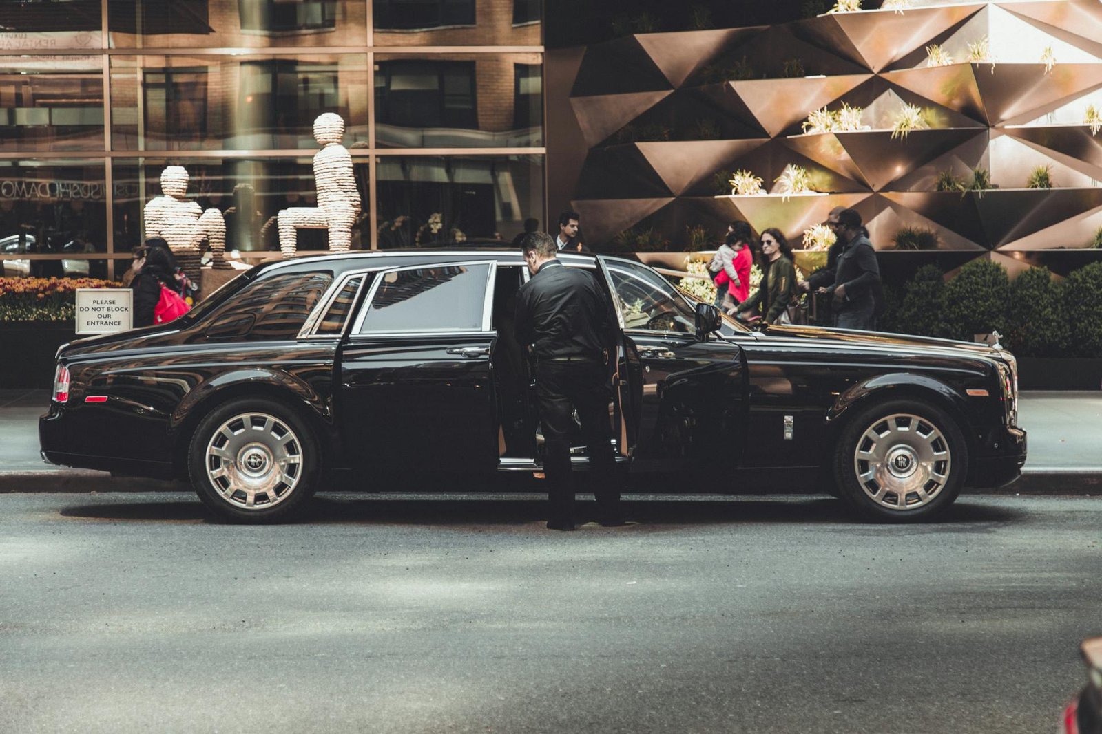 Chauffeur beside a black Rolls-Royce Phantom outside a luxury store for corporate travel