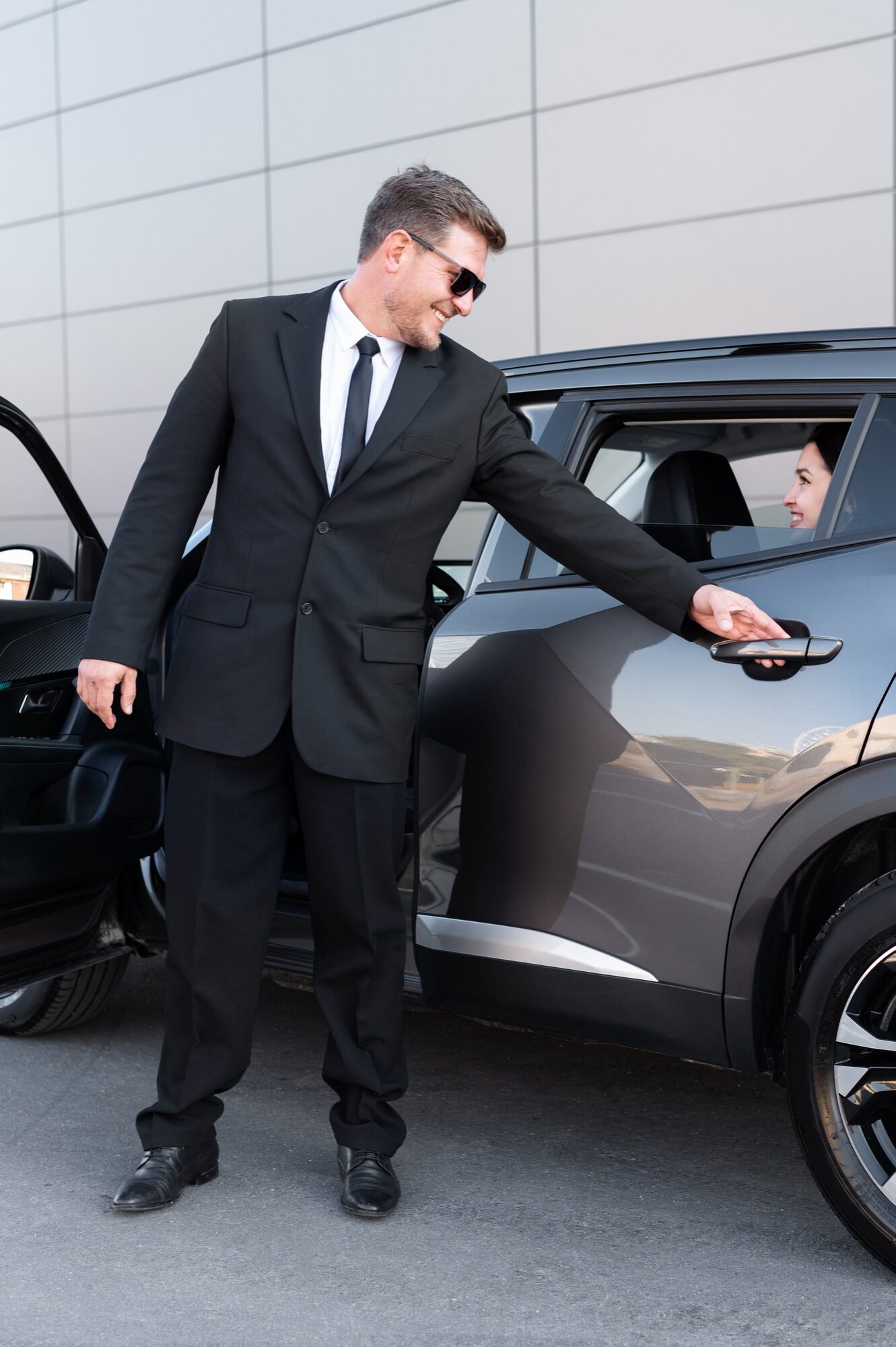 Chauffeur in a suit opening the rear door of a grey SUV for a Royale Rides client