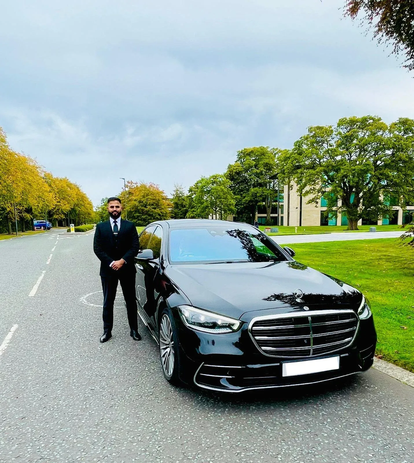 Chauffeur and client beside a black Mercedes on a tree-lined road for Royale Rides chauffeur services