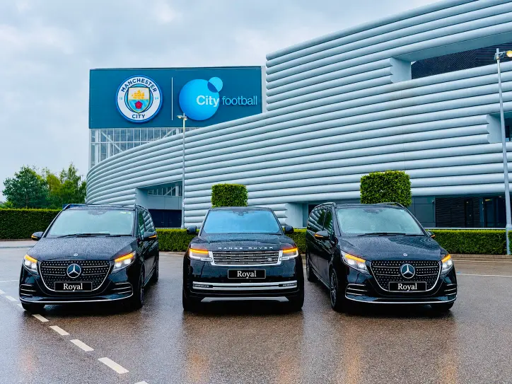 Three black Mercedes V-Class chauffeur vehicles outside the Manchester City stadium store